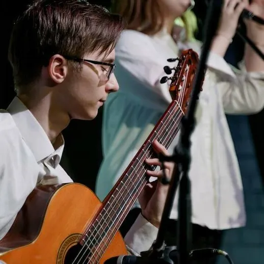 Молодежный концерт в центре города, где юные музыканты исполняют живую музыку на гитаре и поют