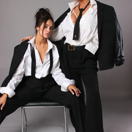 Две модели в стильных черных нарядах позируют на фоне серой стены в студии