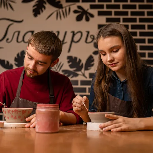 Молодая пара создает керамические изделия в мастерской на фоне кирпичной стены с надписью