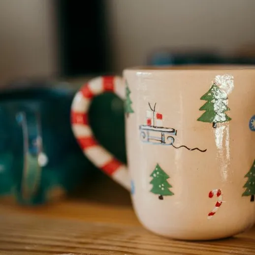 Чашка с новогодним рисунком на фоне рождественских украшений в уютной обстановке дома