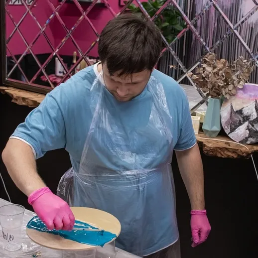 Мастер-класс по созданию эпоксидной смолы в студии, где мужчина смешивает синий цвет, окружённый коллажами