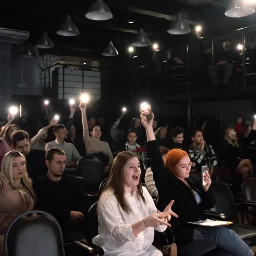 Зрители с поднятыми телефонами на мероприятии в темном зале, атмосфера восторга и поддержки