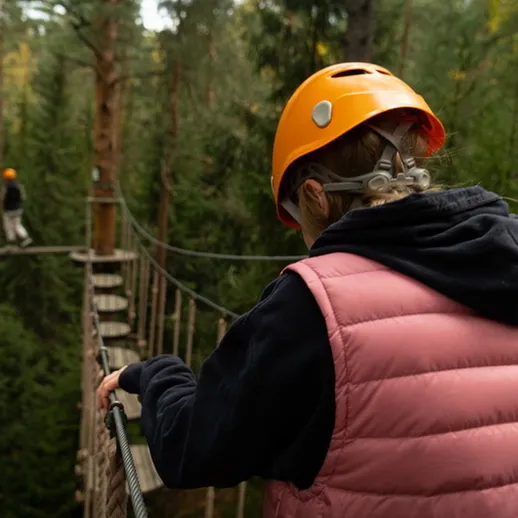 Молодой человек на канатной переправе в лесу, осенью, с защитным шлемом и снаряжением для приключений
