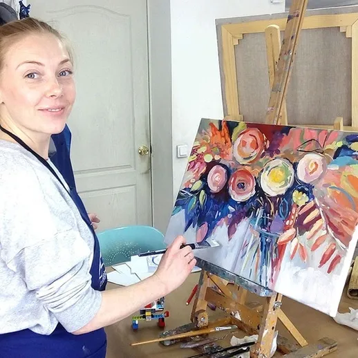 Художник улыбается, работая над ярким натюрмортом с цветами в студии