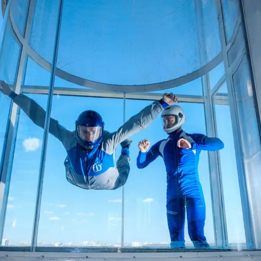 Парашютист в вертикальном аэродинамическом туннеле выполняет трюки под наблюдением инструктора