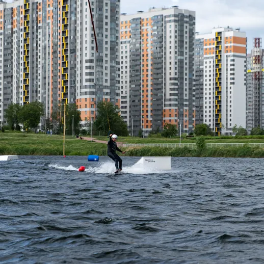 Сноубордист на водных лыжах катится по озеру с современными зданиями на заднем плане