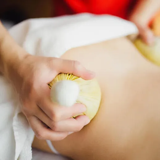 Массаж с использованием травяных мешочков на спине клиента в спа-салоне