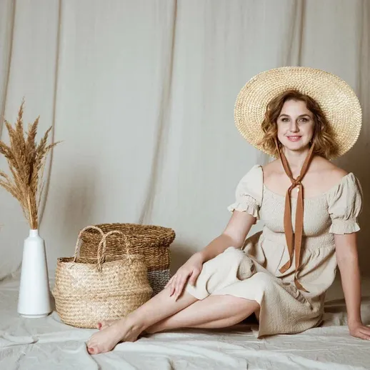 Молодая женщина в летнем платье позирует на фоне нейтральных тканей в уютной обстановке с плетеными корзинами