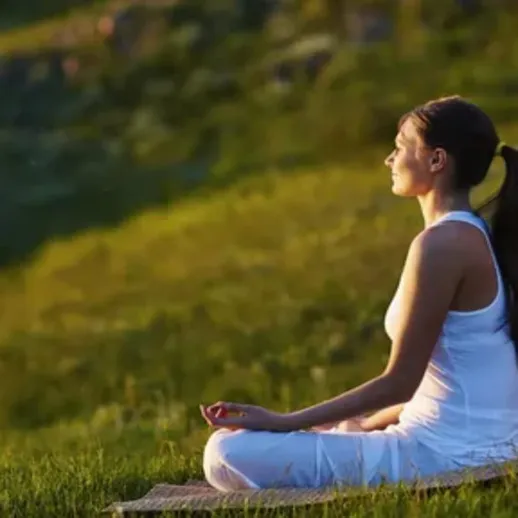 Женщина медитирует на зелёном склоне холма в солнечный день