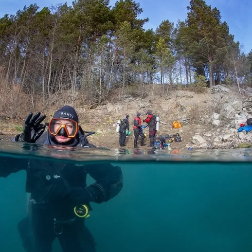Подводные исследования у берега с дайверами в чистой воде озера среди лесных скал в ясный день