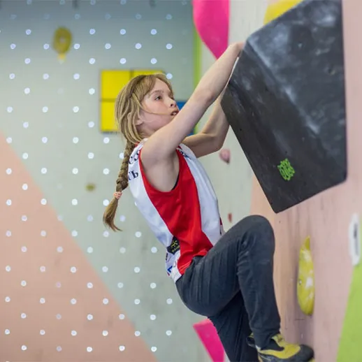 Девочка занимается скалолазанием в спортивном зале с яркими стенами в дневное время