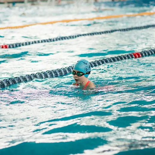 Девочка плавает в бассейне во время тренировки с другими спортсменами в холодное время года