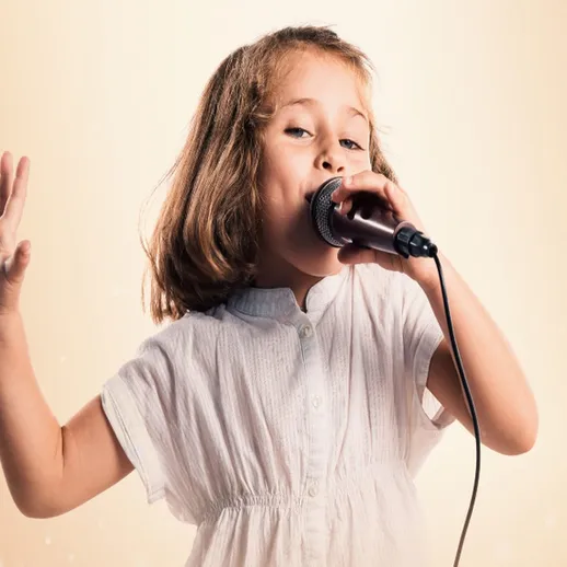 Девочка поет в микрофон на сцене в ярком свете, погружаясь в мир музыки и творчества