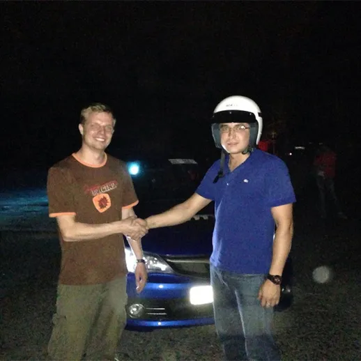 Два человека жмут руки на ночной автодороге после успешного заезда на спортивной машине