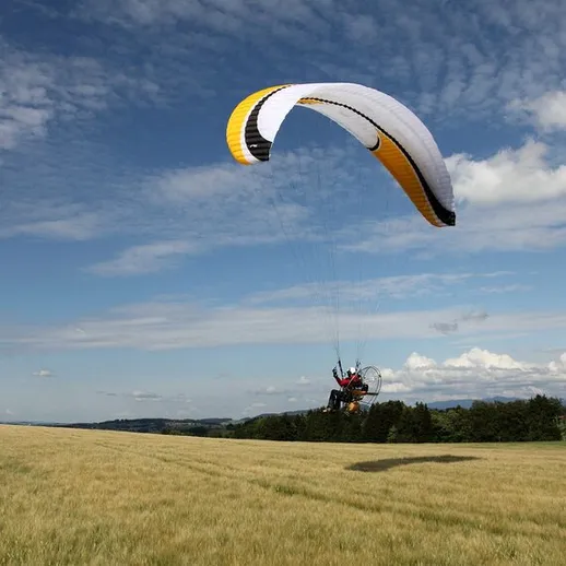 Парапланерист над зелёным полем в солнечный день с облаками на фоне