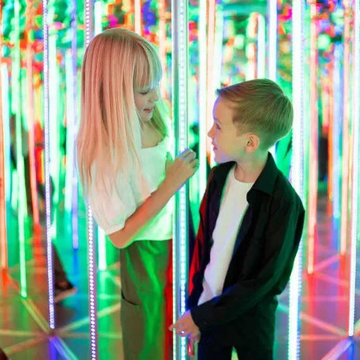 Дети в светящемся лабиринте, играющие и смеющиеся среди ярких неоновых огней в развлекательном центре