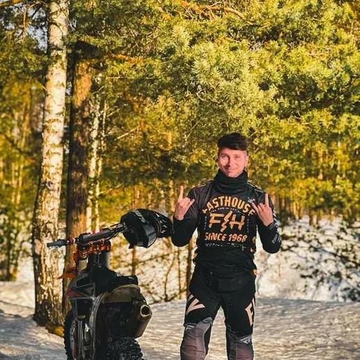 Молодой человек с мотоциклом на зимней лесной дороге, позирующий с жестом в знак признания и дружбы