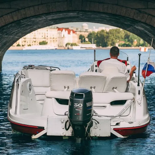 Человек на моторной лодке проходит под мостом в спокойной реке на фоне города