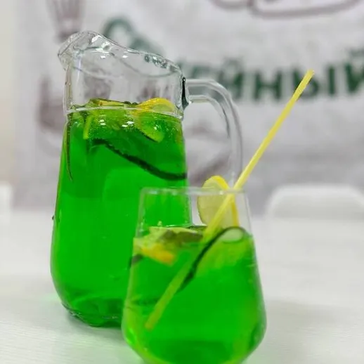 Яркий зеленый напиток с лимоном в кувшине и стакане на столе