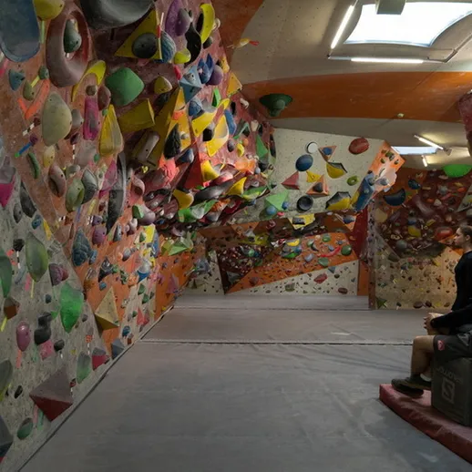 Закрытый скалодром с разнообразными маршрутами для боулдеринга и отдыхающей группой на фоне желтых и красных стен