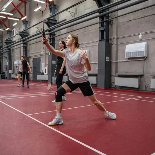 Женщина играет в бадминтон в спортивном зале, тренируя свои навыки и технику в переменчивом темпе