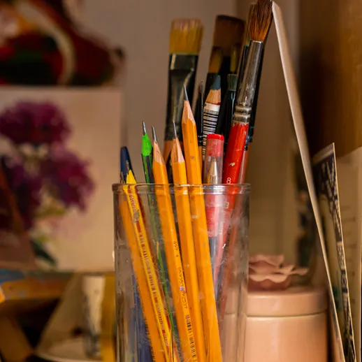 Стеклянная банка с кистями и карандашами на полке в мастерской поздним вечером