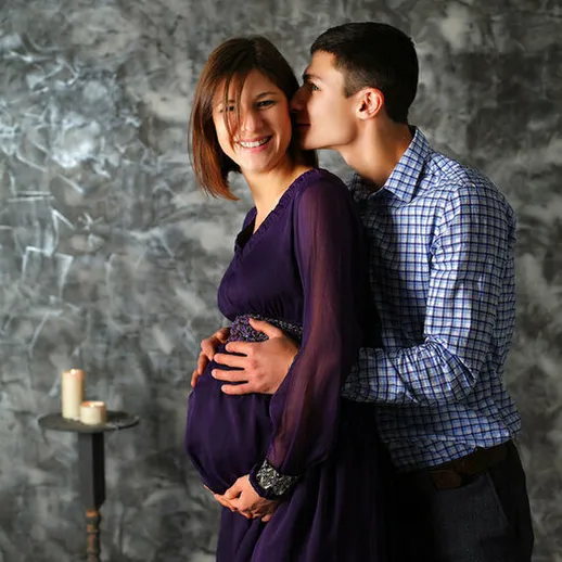 Счастливая пара ждет ребенка на фотосессии в интерьере с серой стеной и свечами