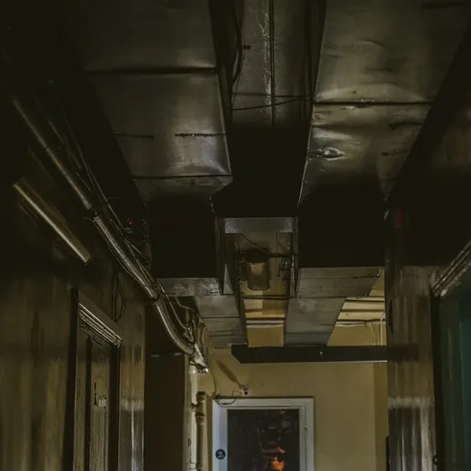Темный коридор с высокими потолками в заброшенном здании, обветшалые стены и провода на потолке, вечернее время