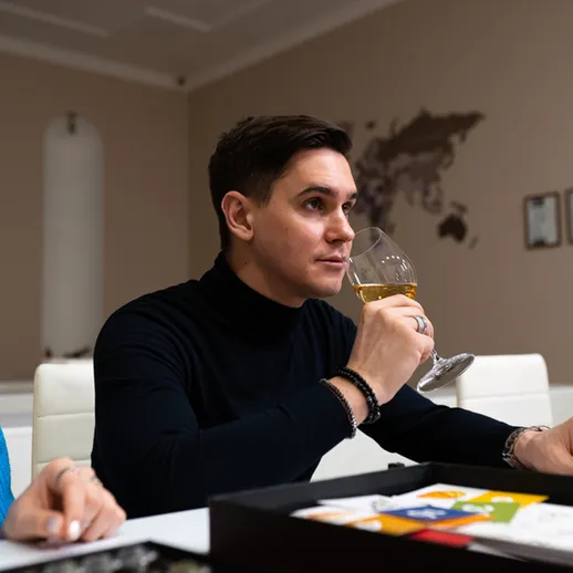 Молодой человек с бокалом вина за столом, увлеченно играющий в настольную игру в комфортабельном интерьере