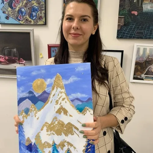 Молодая женщина демонстрирует картину с горами в художественной галерее в городе