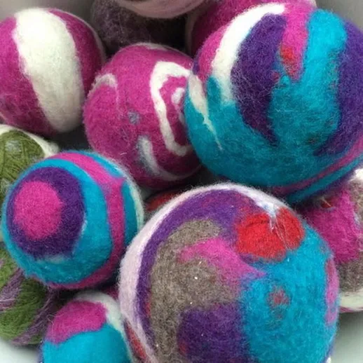 Яркие валяные шары разных размеров в белой миске, украшенные разноцветными узорами и текстурами