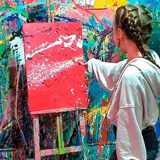 Девушка создает абстрактную картину на фоне яркой стены с красками в художественной студии