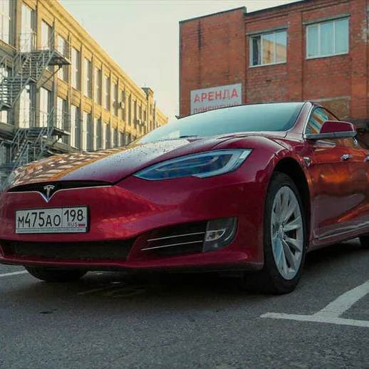 Красный электромобиль припаркован на пустой стоянке во дворе старого здания в солнечный день