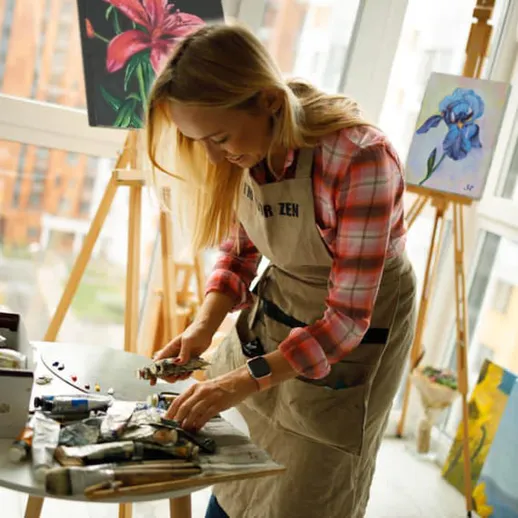 Художник работает над картинами в светлой студии с окнами в современном районе города