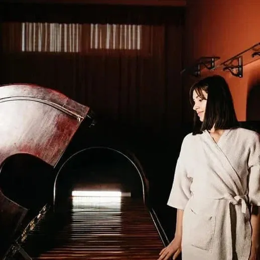 Женщина в халате стоит рядом с уникальным деревянным инструментом в уютном помещении с мягким освещением