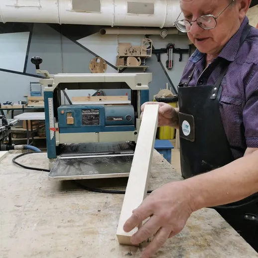 Мастерская деревообработки: пожилой мужчина работает с древесиной у фрезера в мастерской