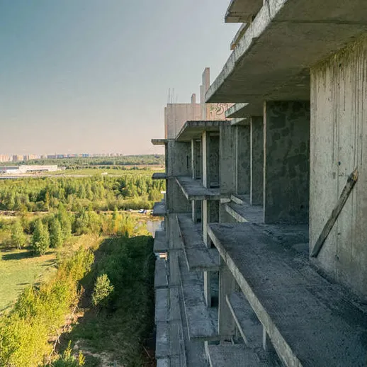 Заброшенное строительное здание на фоне зелёной природы и городского пейзажа на закате