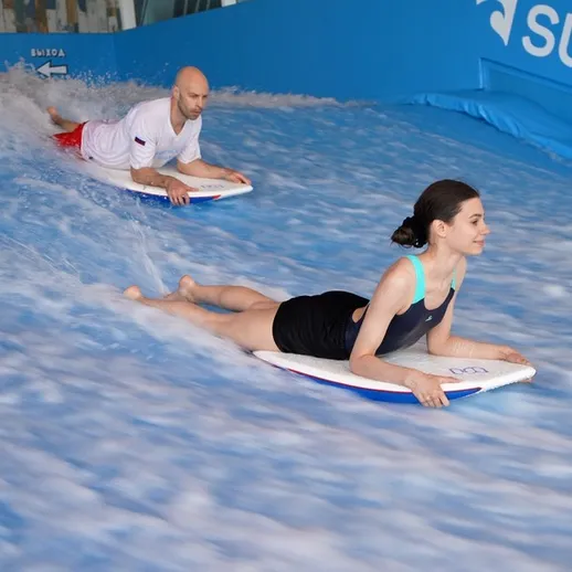 Два человека катаются на досках в серфинговом центре под крышей в зимний день