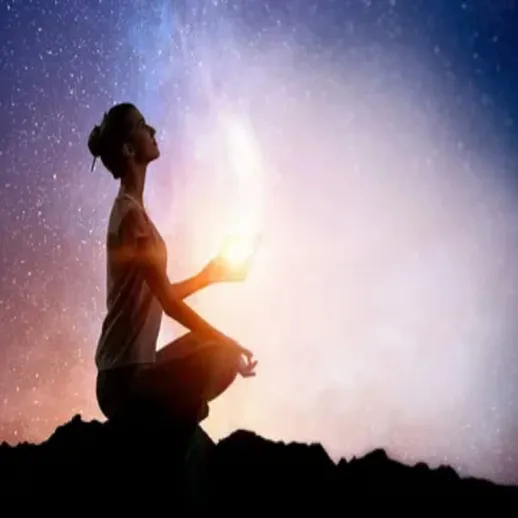 Женщина медитирует на скале под звёздным небом в спокойной атмосфере ночи, создавая ауру света вокруг себя