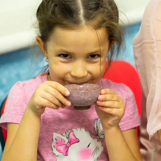 Девочка в розовой футболке держит керамическую чашку и улыбается на мастер-классе по гончарному делу