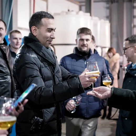 Сотрудники предприятия празднуют юбилей в производственном цехе с кружками пива и хорошим настроением