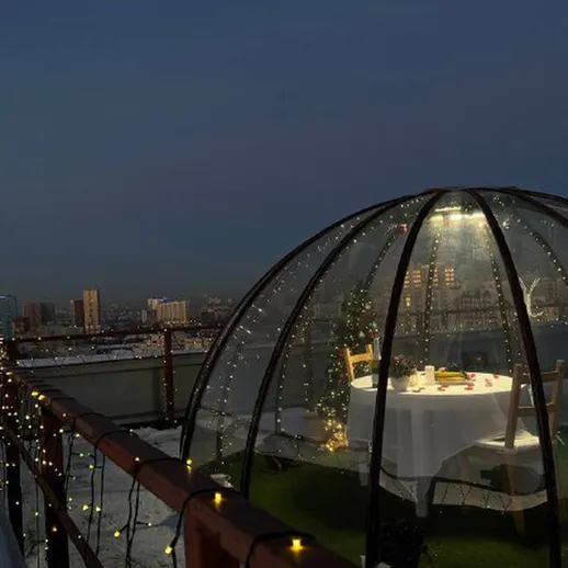 Уютный обед под звездами в прозрачном куполе на крыше города в зимний вечер