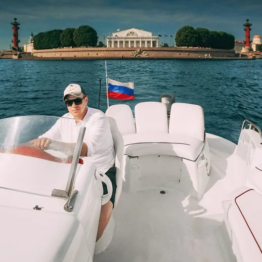 Капитан на лодке в центре Санкт-Петербурга с видом на Эрмитаж и Неву в ясный день
