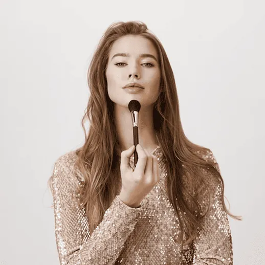 Женщина с кисточкой для макияжа наносит косметику на лицо в стильной одежде