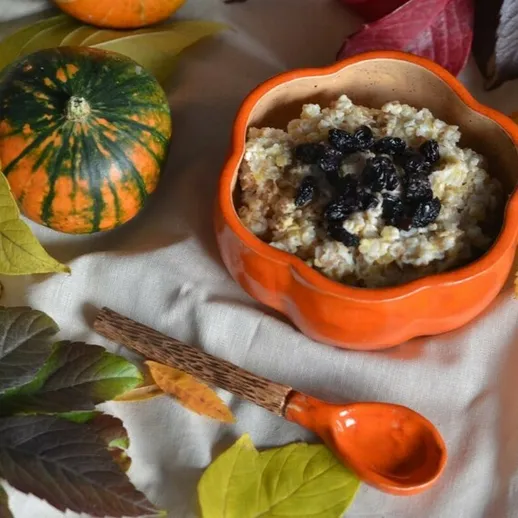 Овсянка с черными ягодами в оранжевой тарелке на фоне осенних листьев и тыквы