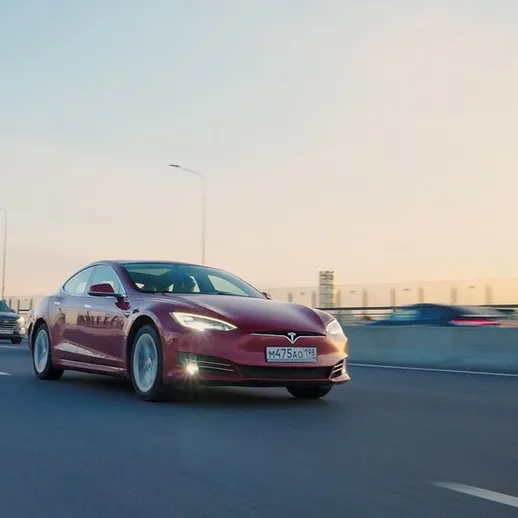 Красный электромобиль движется по дороге на фоне вечернего заката, городская атмосфера, спокойный трафик