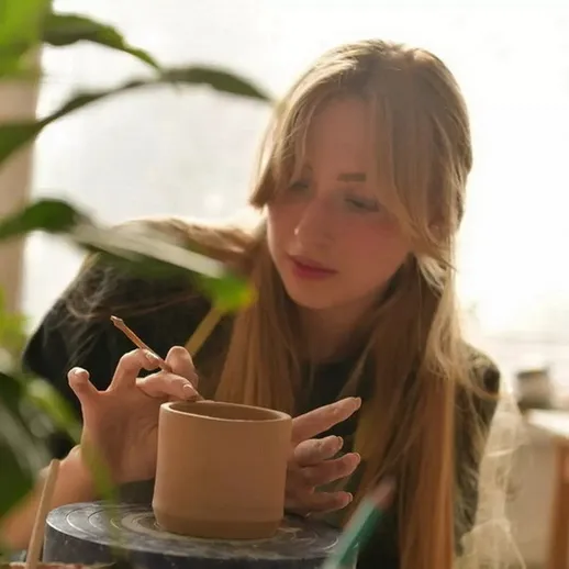 Молодая женщина создает керамическое изделие в мастерской с зелеными растениями и мягким светом