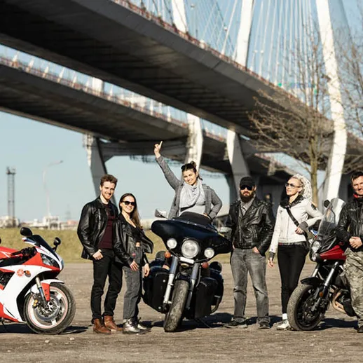 Группа мотоциклистов позирует на фоне моста в солнечный день