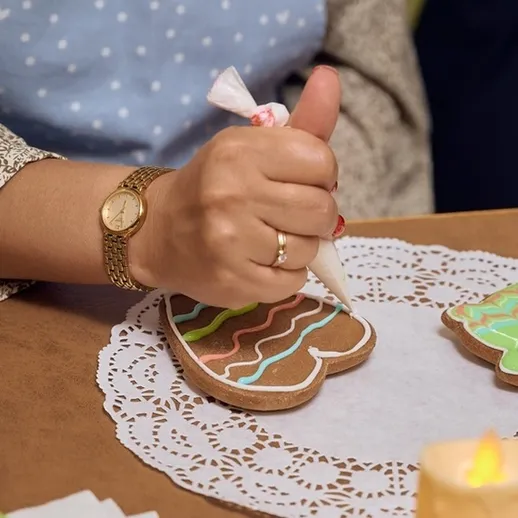 Женщина украшает имбирные пряники на столе с кружевной салфеткой в уютной атмосфере вечером