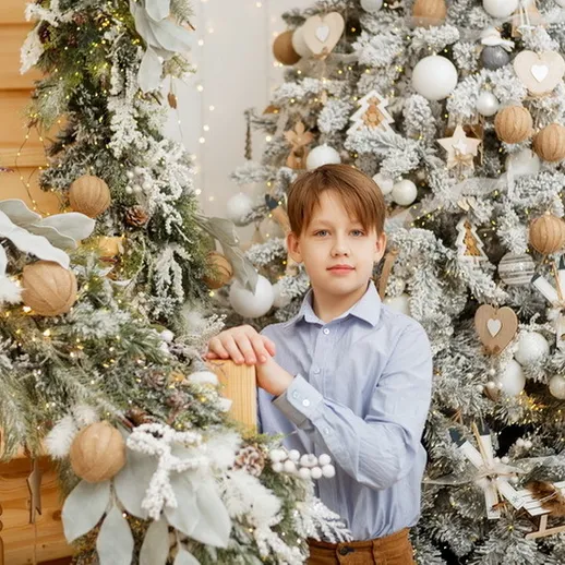 На празднике: мальчик у новогодней елки с украшениями в уютном доме
